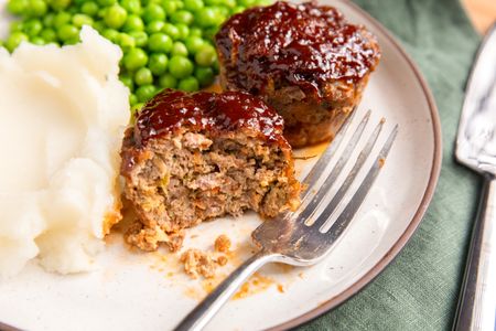 Meatloaf muffins served on a plate with peas and mashed potatoes