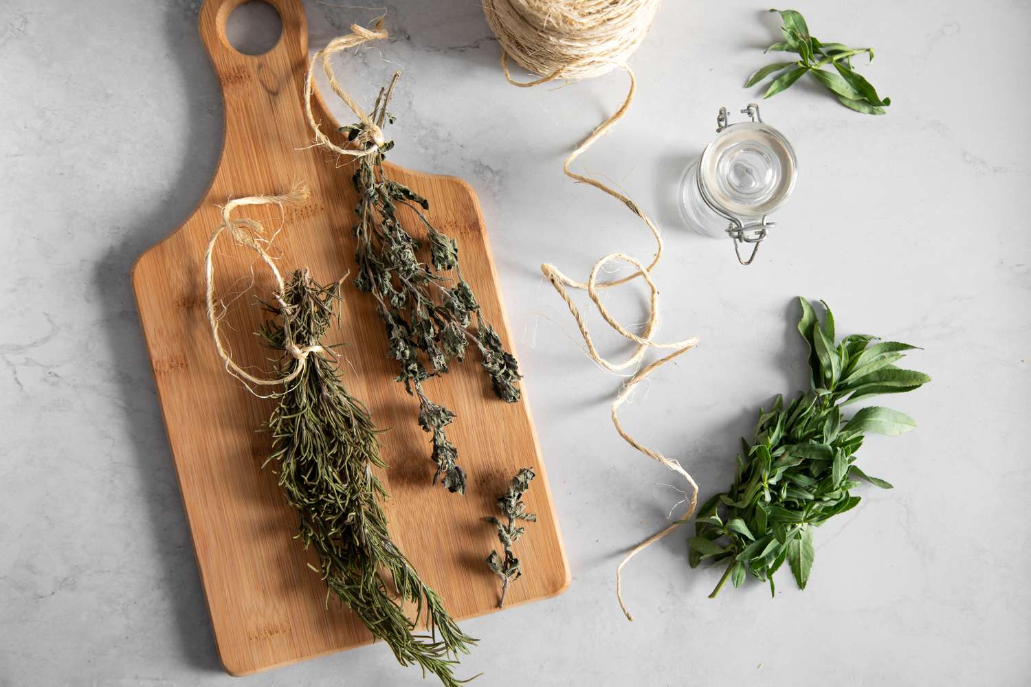 Sprigs of Dried Herbs on a Wooden Cutting Board Next to More Fresh Herbs and a Roll of Twine