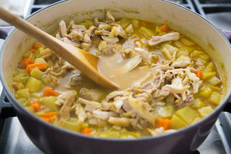Shredded chicken added to Mulligatawny soup in a Dutch Oven with a spoon