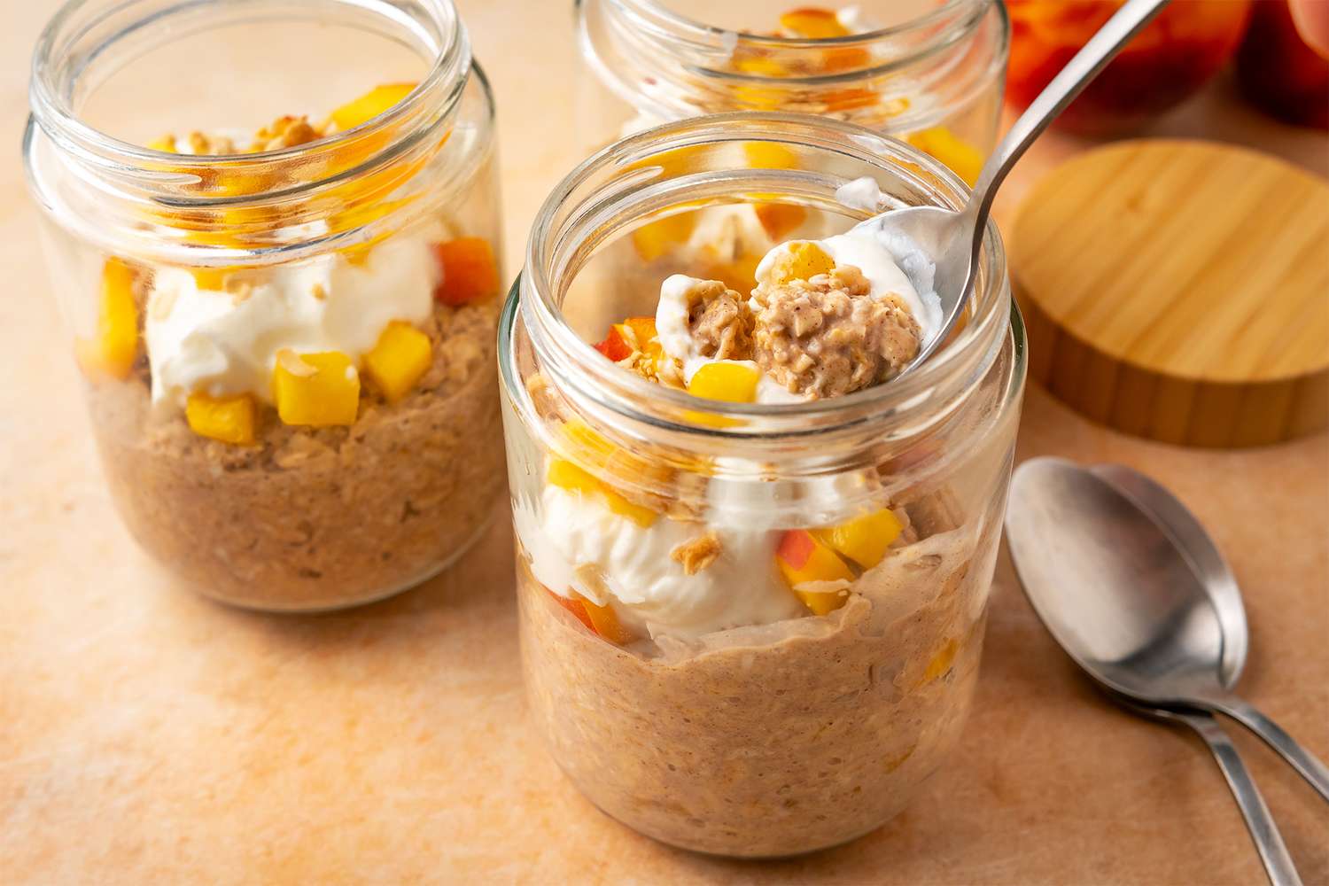 Jars of peach cobbler overnight oats topped with fruit and cream