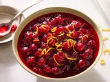 A bowl of cranberry sauce garnished with lemon zest with a spoon in the background