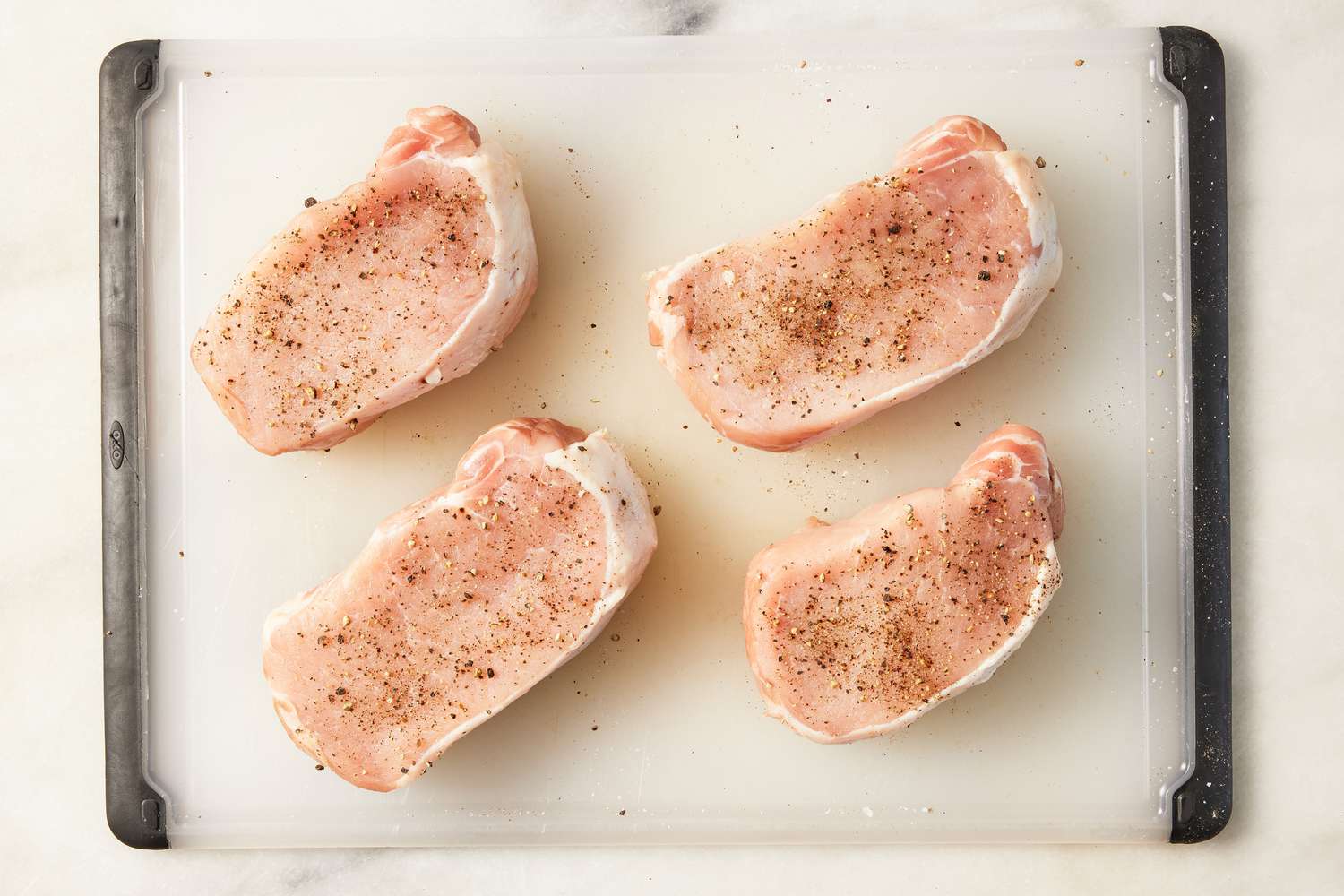 pork chops seasoned with salt and pepper on a cutting board for glazed pork chops recipe