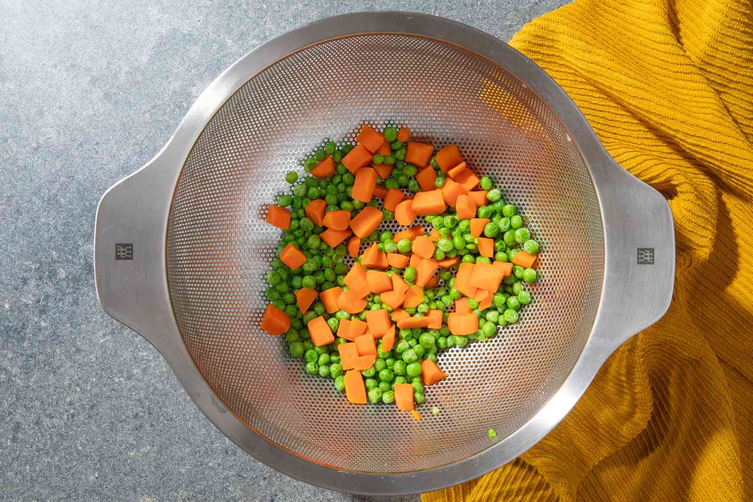 cooked peas and carrots in a colander for olivier potato salad recipe