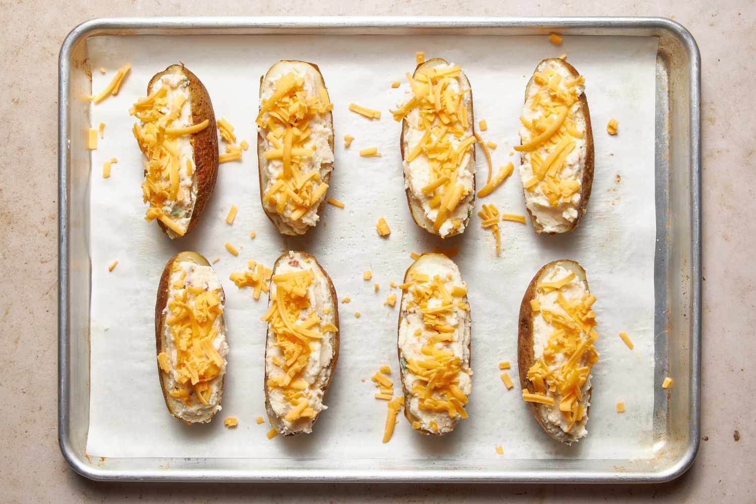 Potato skins filled with filling and topped with shredded cheddar on a parchment paper-lined baking sheet for twice baked potatoes recipe