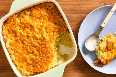 Overhead view of a square white baking dish of potato cabbage casserole next to a light blue plate with a casserole serving and spoon all on a wooden tabletop