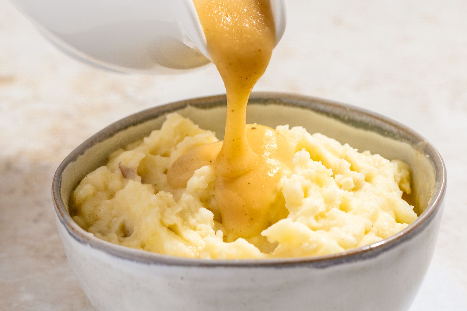 Side view of pouring gravy from a gravy boat onto a bowl of mashed potatoes