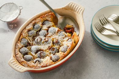Cherry clafoutis served in a baking dish with a serving spoon, plates and forks are set nearby