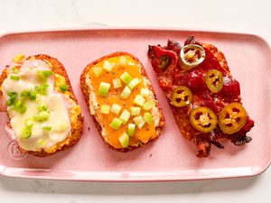 Three hashbrown patties topped with a variety of ingredients presented on a pink platter