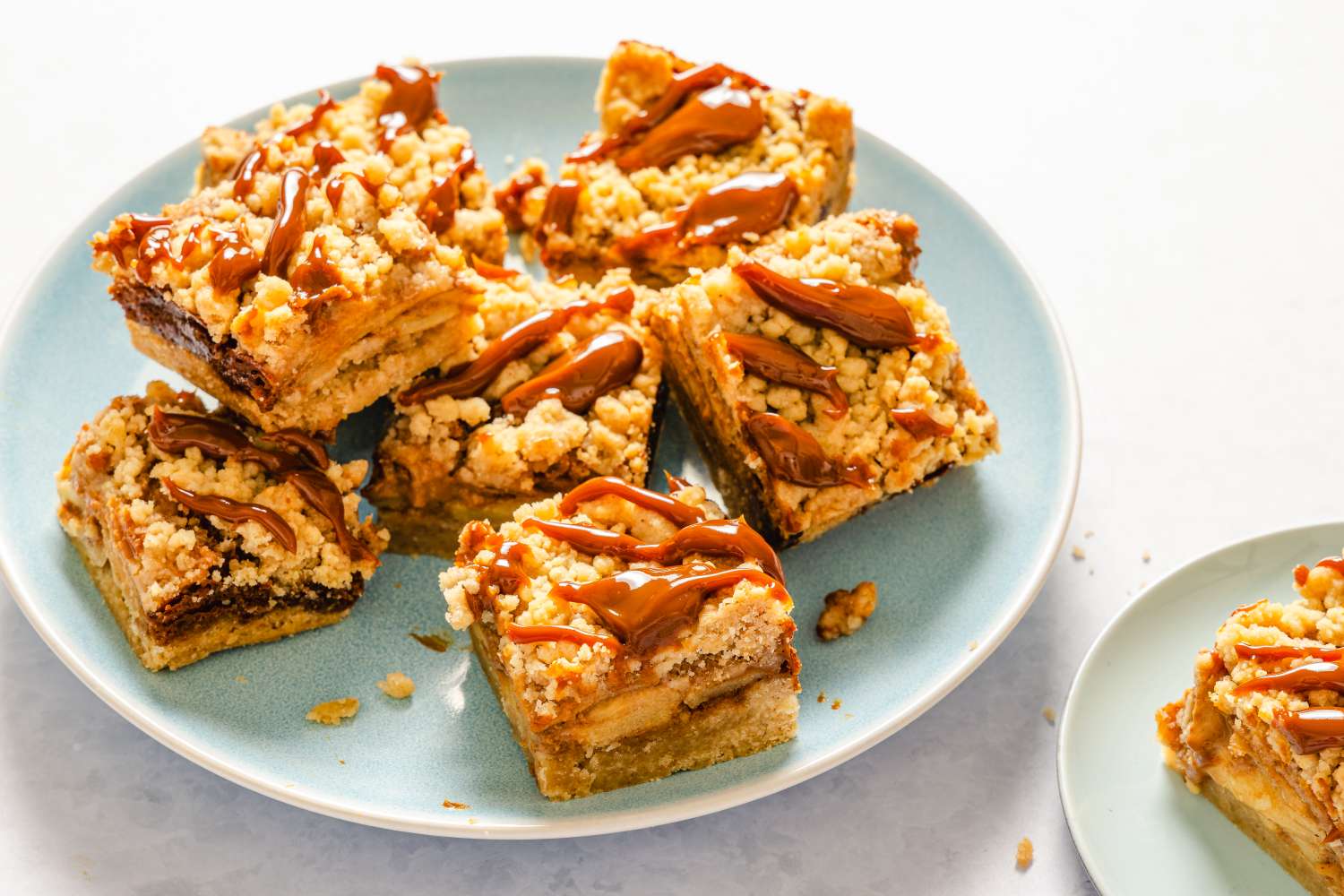 Plate of caramel apple bars topped with drizzle and crumble served on light blue plates