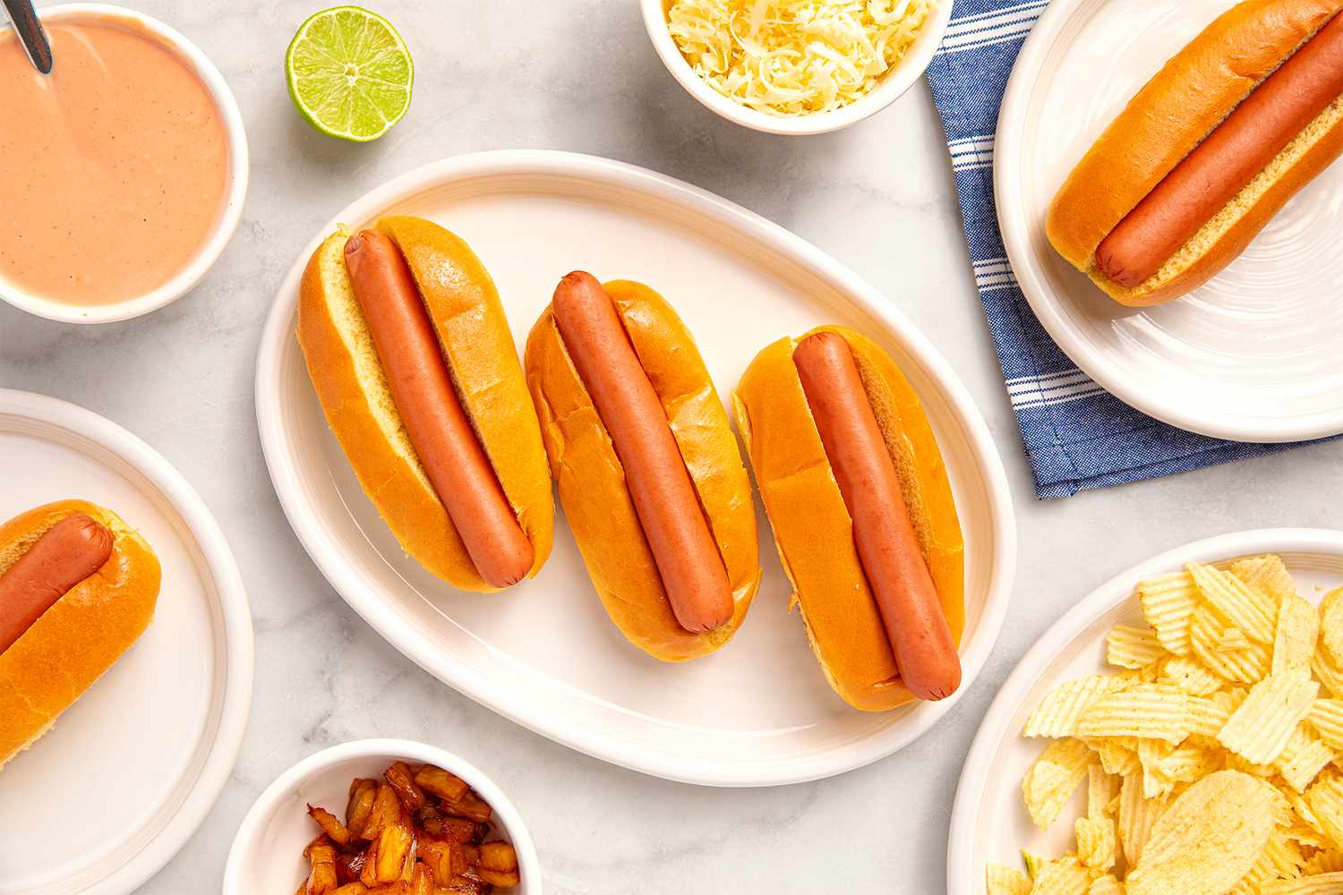 Four hot dogs in buns on a platter surrounded by toppings and sides