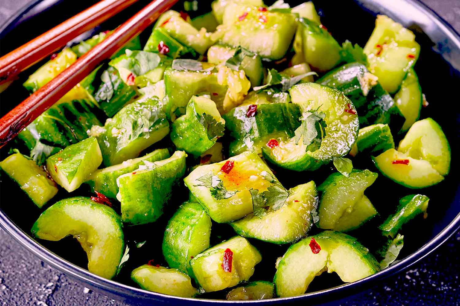 A dish of chopped cucumbers seasoned with herbs and spices served in a bowl with chopsticks