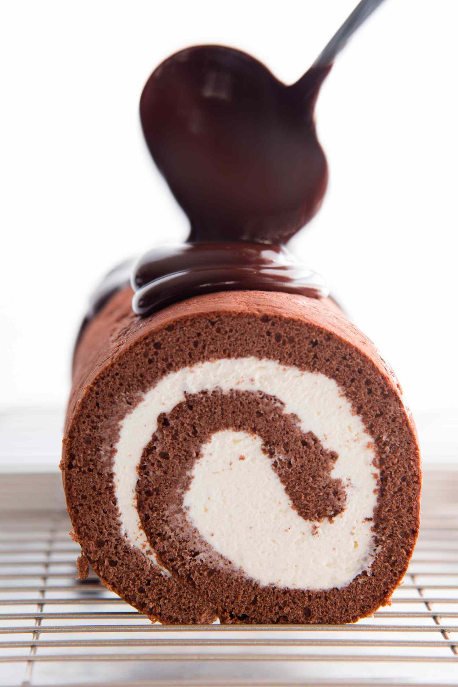 Side view of a chocolate swiss roll with ganache being poured over top.
