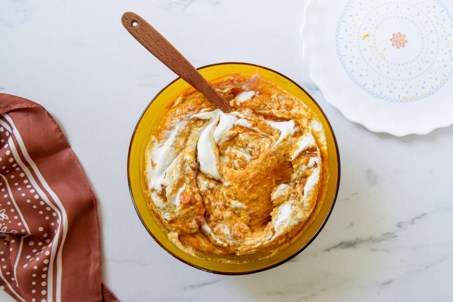 Whipped cream and pumpkin puree folded together using a spatula in a bowl next to a browl kitchen linen for 2-ingredient pumpkin mousse recipe
