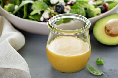 Jar of creamy salad dressing beside an avocado and a bowl of salad
