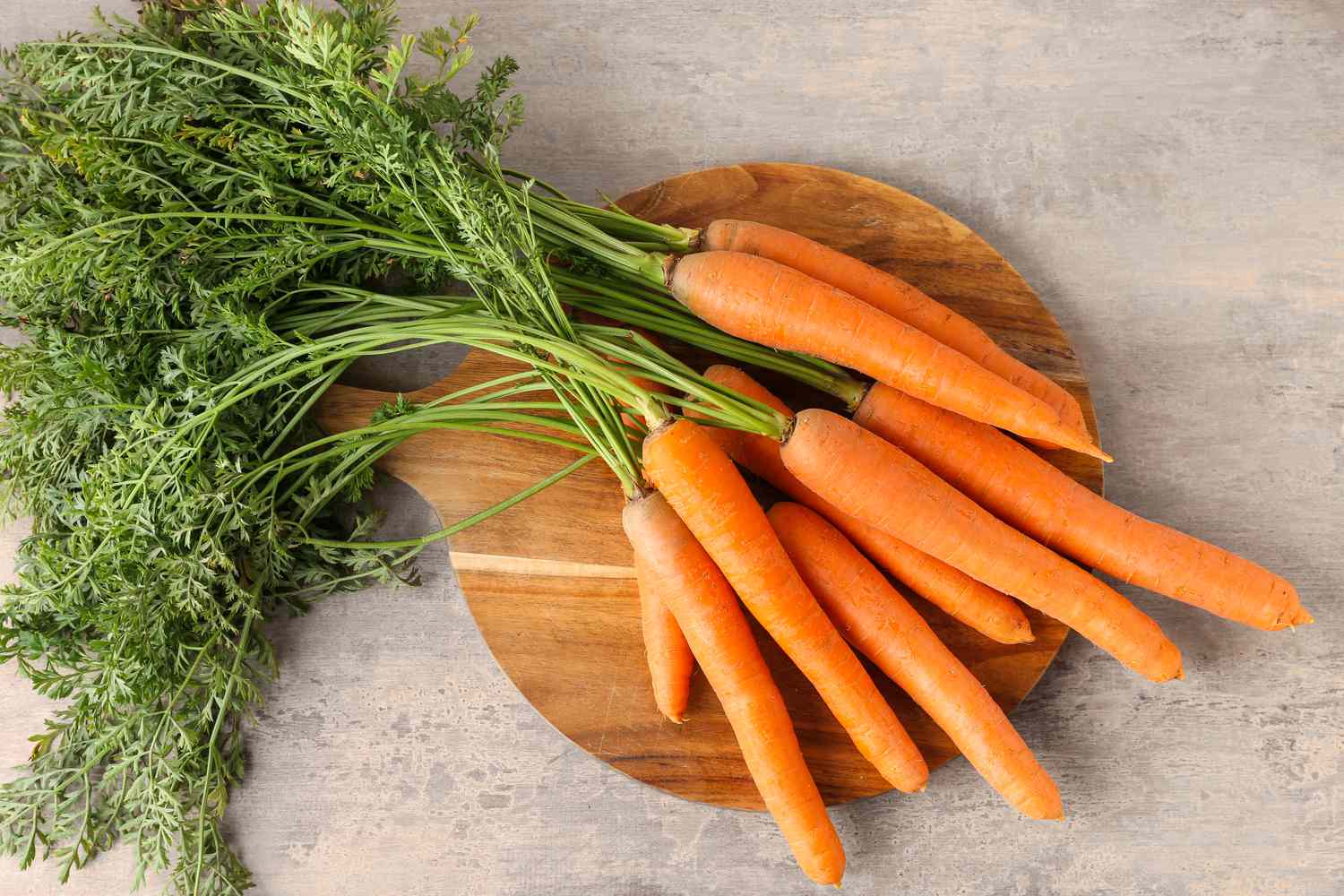 Overhead shot of a bunch of fresh carrot on a round wooden cutting board