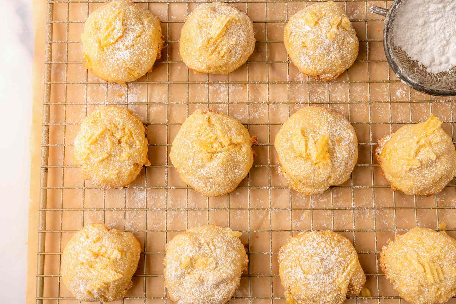 Overhead view of potato chip cookies on a cooling rack over parchment paper next to a owl of powdered sugar