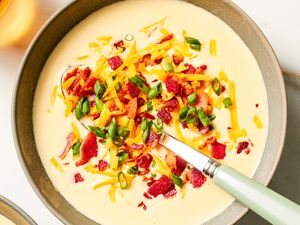 Bowl of loaded potato soup garnished with shredded cheese scallions and bacon with a spoon