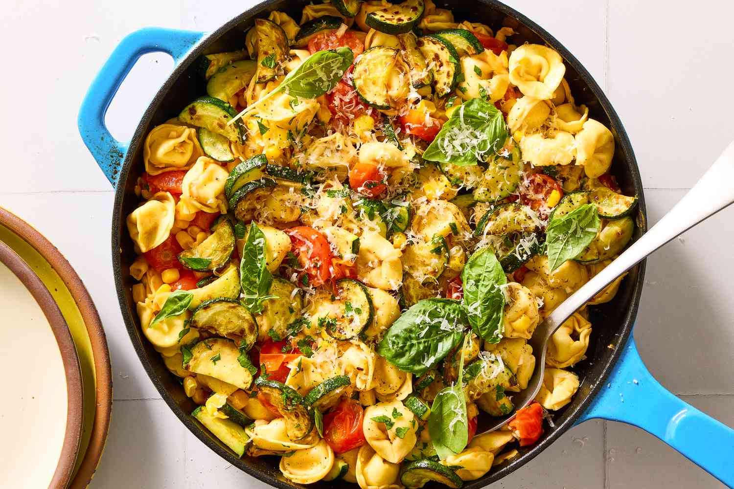 A skillet with tortellini, zucchini, tomatoes, basil, and cheese