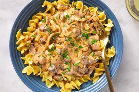 A plate of mushroom stroganoff served over egg noodles garnished with parsley with a fork on the side