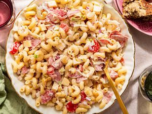ginder pasta salad in a bowl with serving utensils at a table setting with glasses of water, a table napkin, and a stack of plates (close-up)