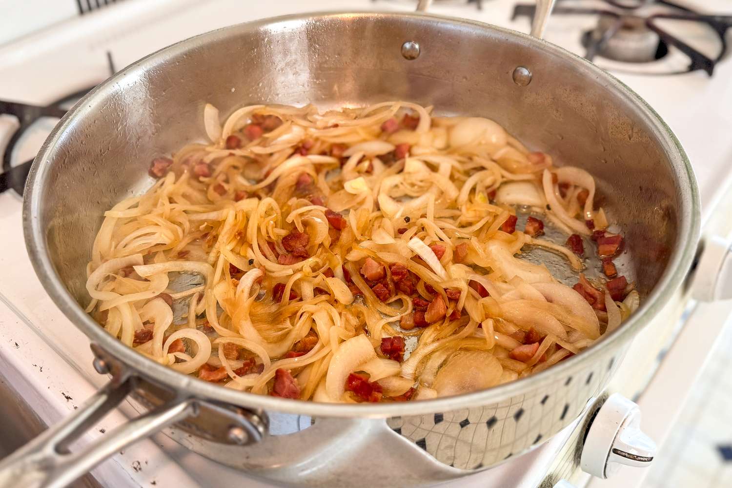 Sauted onions and bacon cooking in a stainless steel pan on a stove