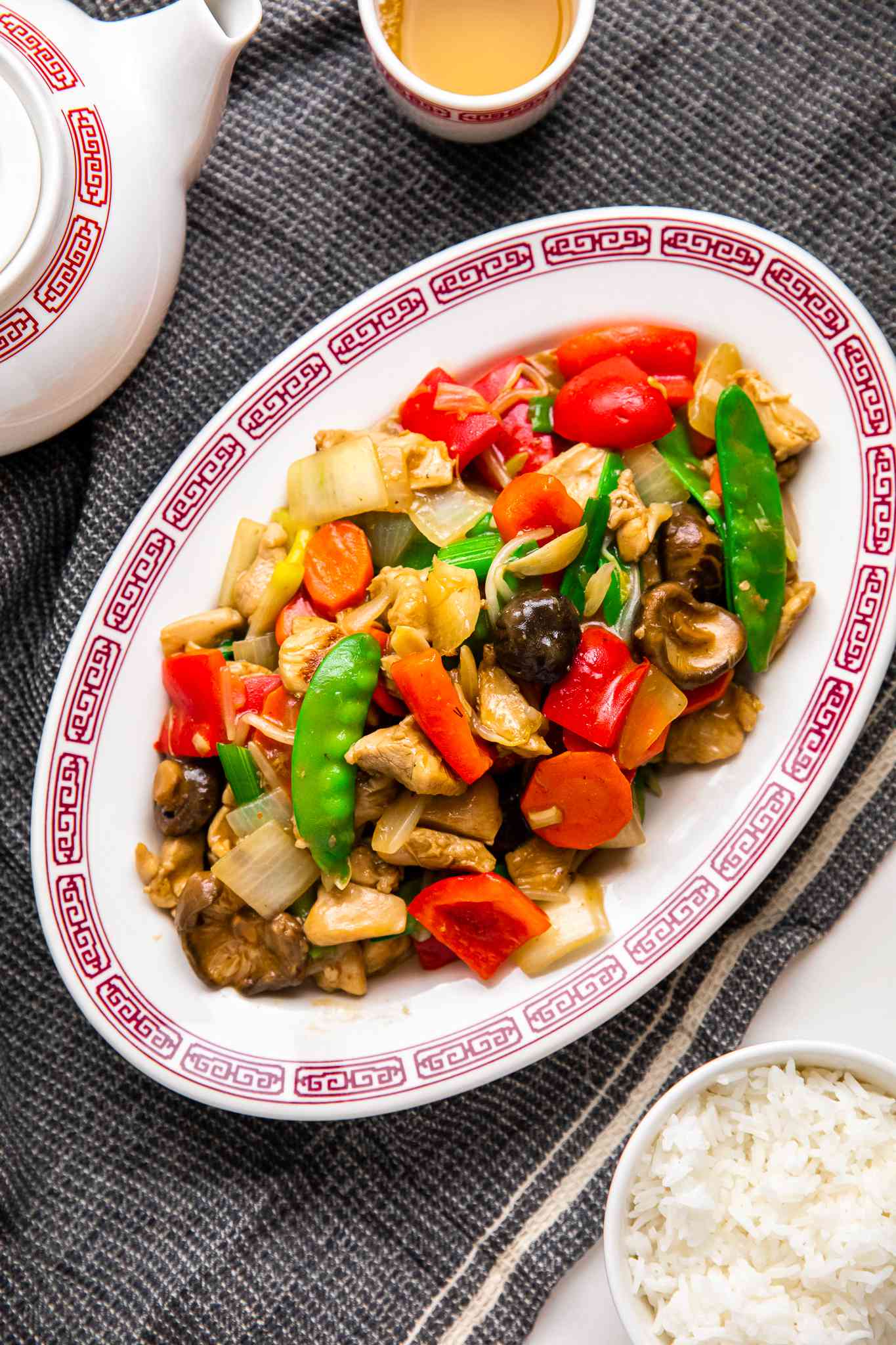 Platter of Chop Suey at a Table Setting With a Bowl of Rice, a Teapot, and a Cup Filled With Tea, All on a Grey Kitchen Towel 
