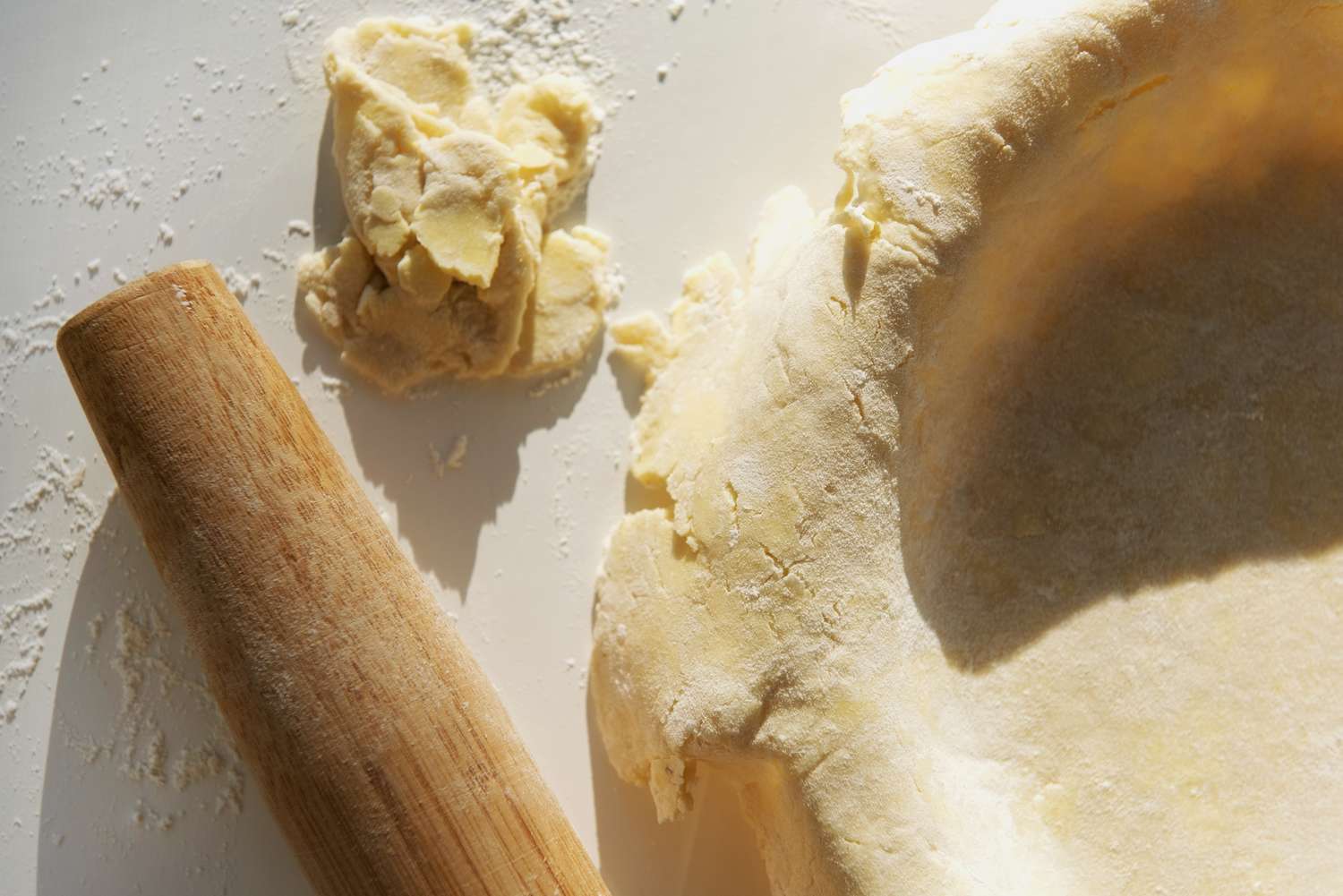 Pie crust being prepared next to dough and a rolling pin