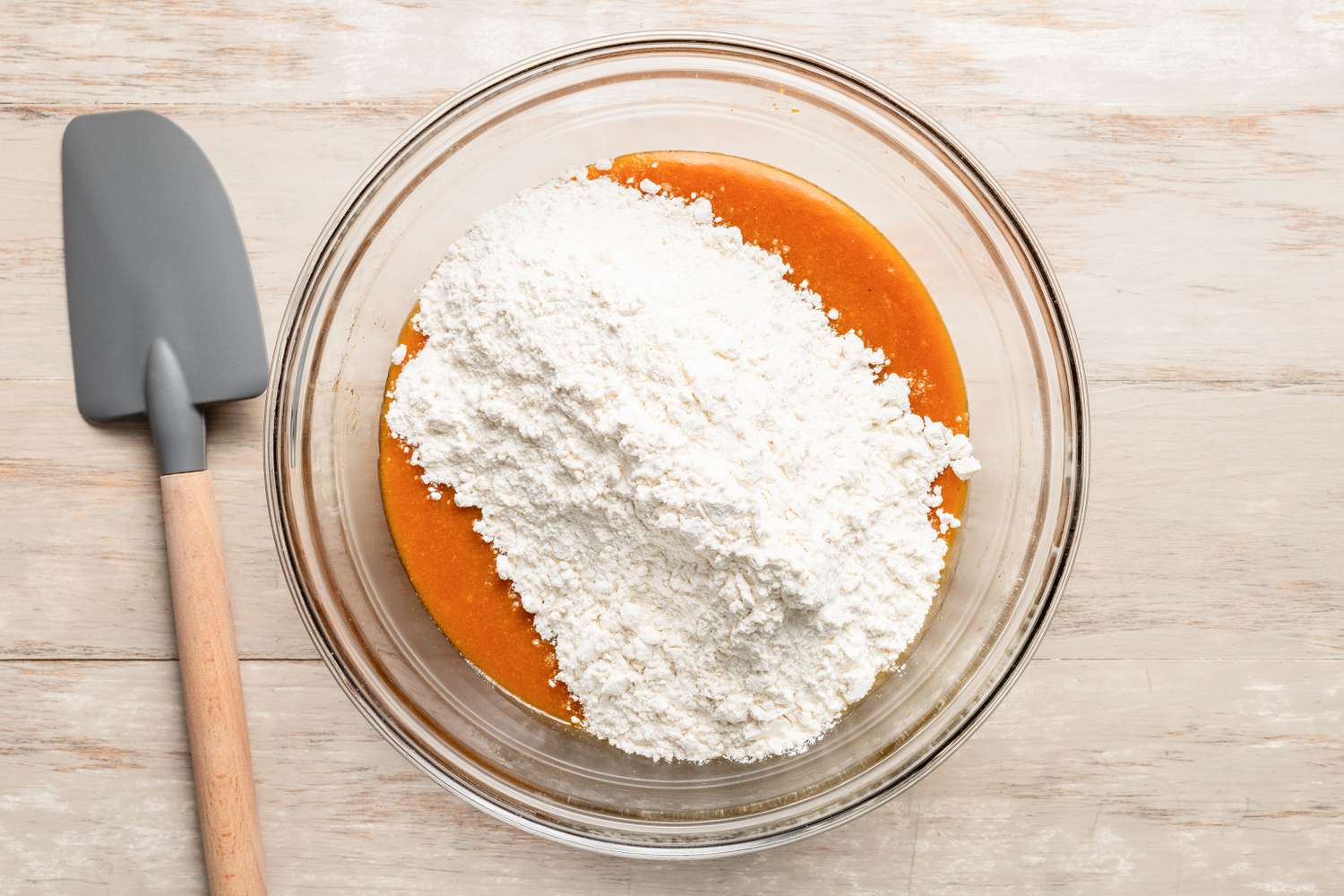 Dry ingredients added to bowl of wet ingredients, and on the counter next to the bowl, a rubber spatula for pumpkin spice cookie recipe