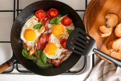 Over easy eggs cooking in a skillet with bacon and halved small tomatoes