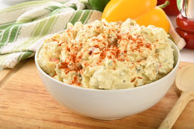 Bowl of sweet potato salad with paprika sprinkle placed on a wooden board