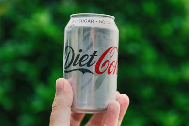 A person holding a can of Diet Coke with a blurred foliage background