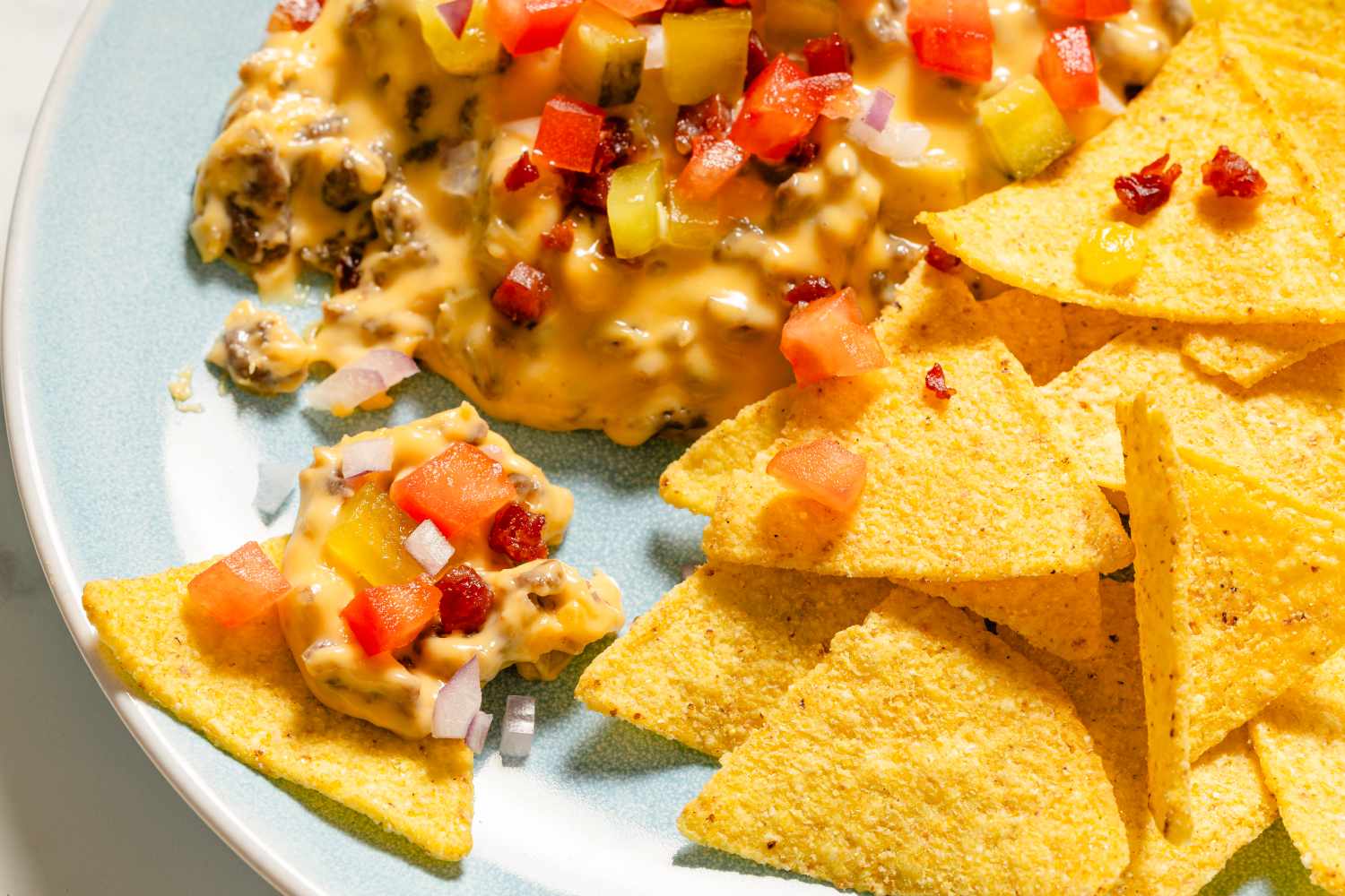 A plate with tortilla chips and a cheesy dip garnished with diced vegetables
