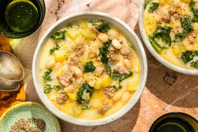 Overhead shot of two bowls with a cream based soup with beans, sausage, kale and potatoes