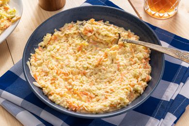 copycat KFC coleslaw in a bowl at a table setting with a glass of iced tea, a pepper grinder, and a plaid table napkin