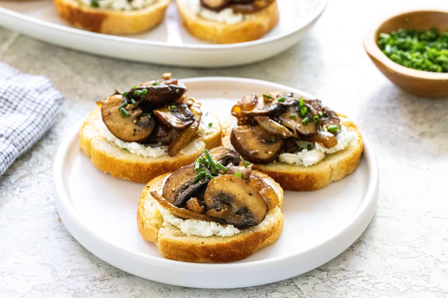 Three crostini topped with savory mushrooms and caramelized onions on a white plate.