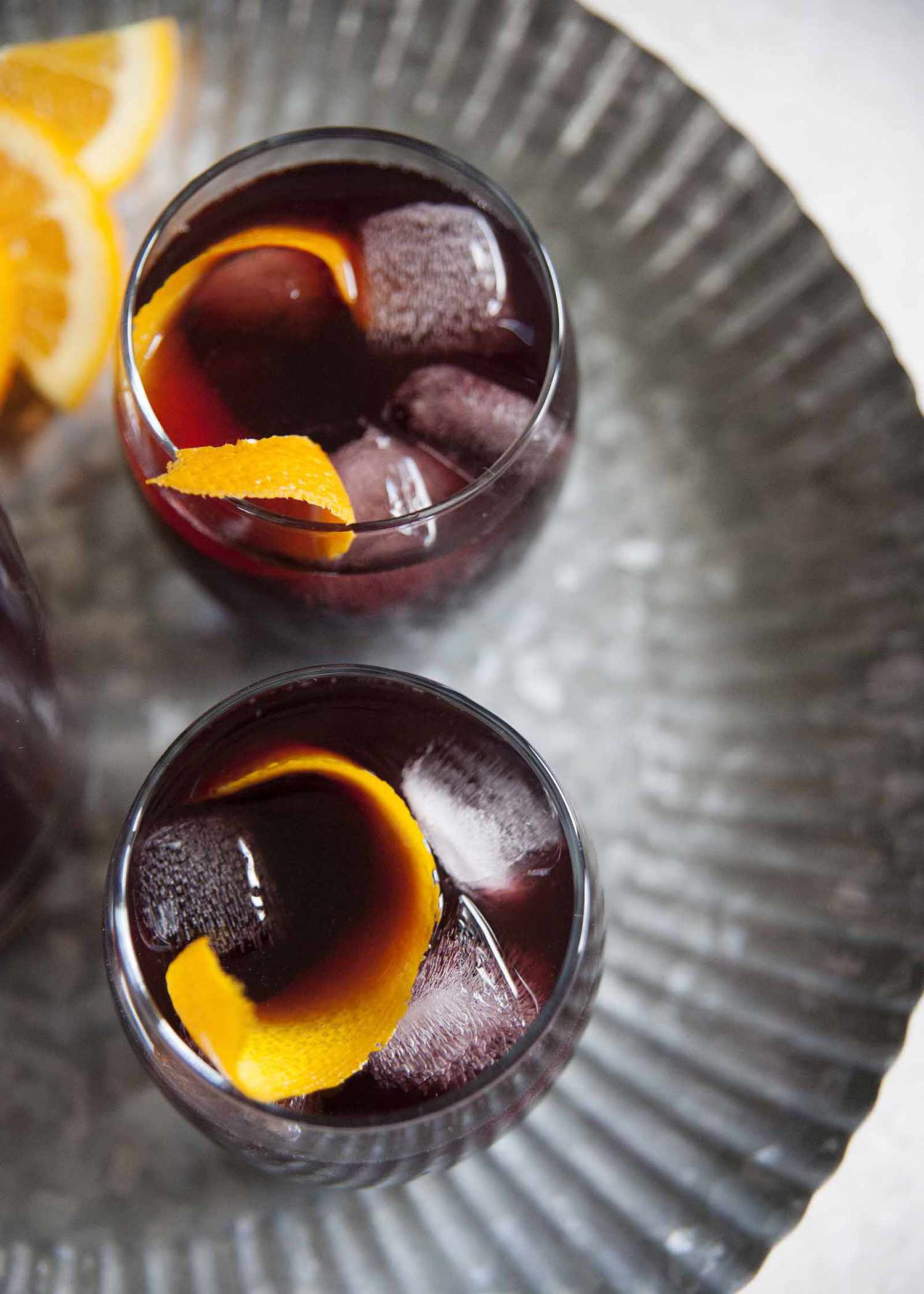 Best Sangria Recipe - orange slices in a pitcher of sangria on a silver tray with two poured glasses of sangria