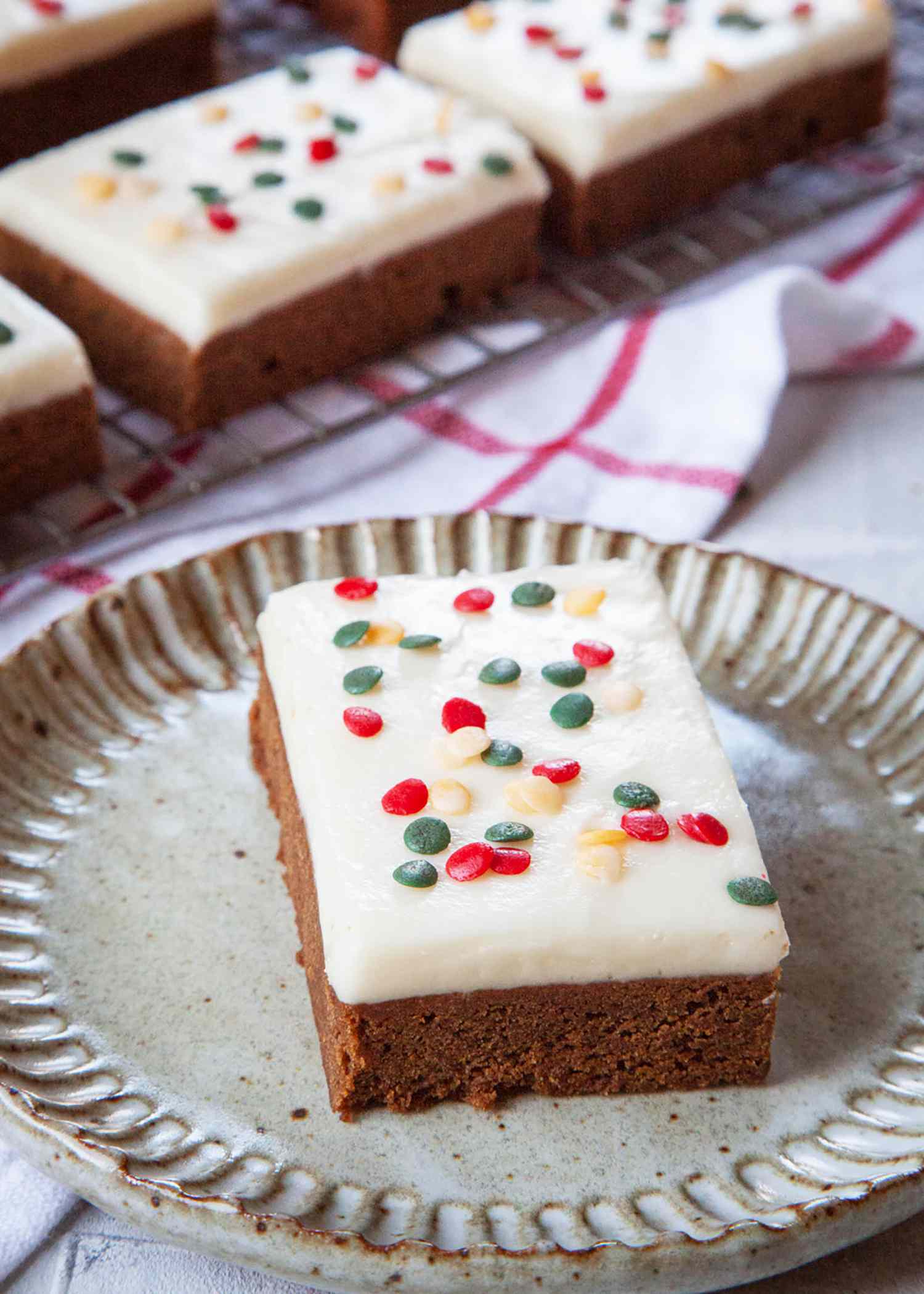 Easy Gingerbread Bars on a plate and topped with a layer of cream cheese frosting and decorated with sprinkles.
