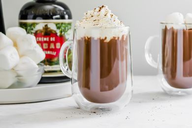 Boozy Hot Chocolate Topped with Whipped Cream and in the Background, a Bowl of Marshmallows and Creme Liqueur
