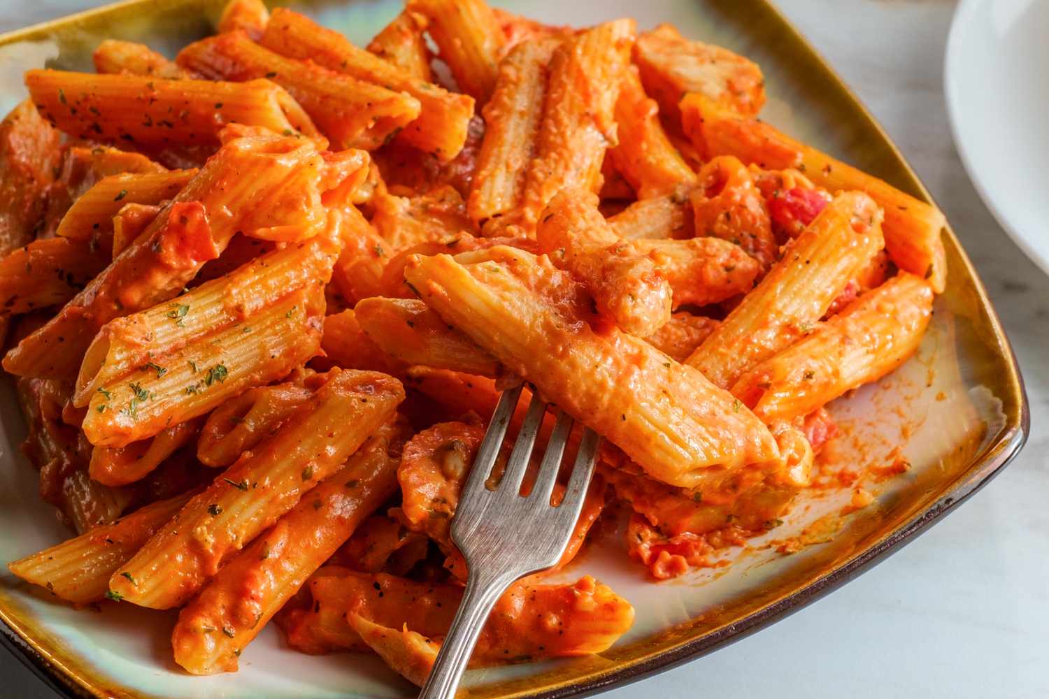 A plate of penne pasta in a creamy tomato sauce with a fork