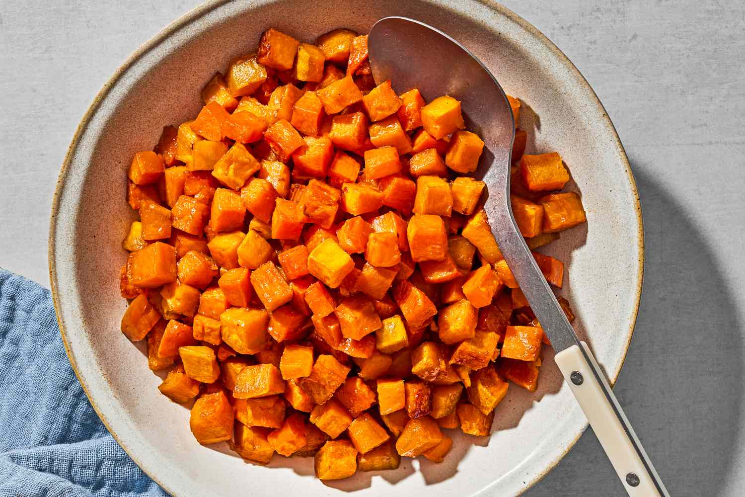 Small cubes of roasted sweet potato in a serving bow, with a serving spoon