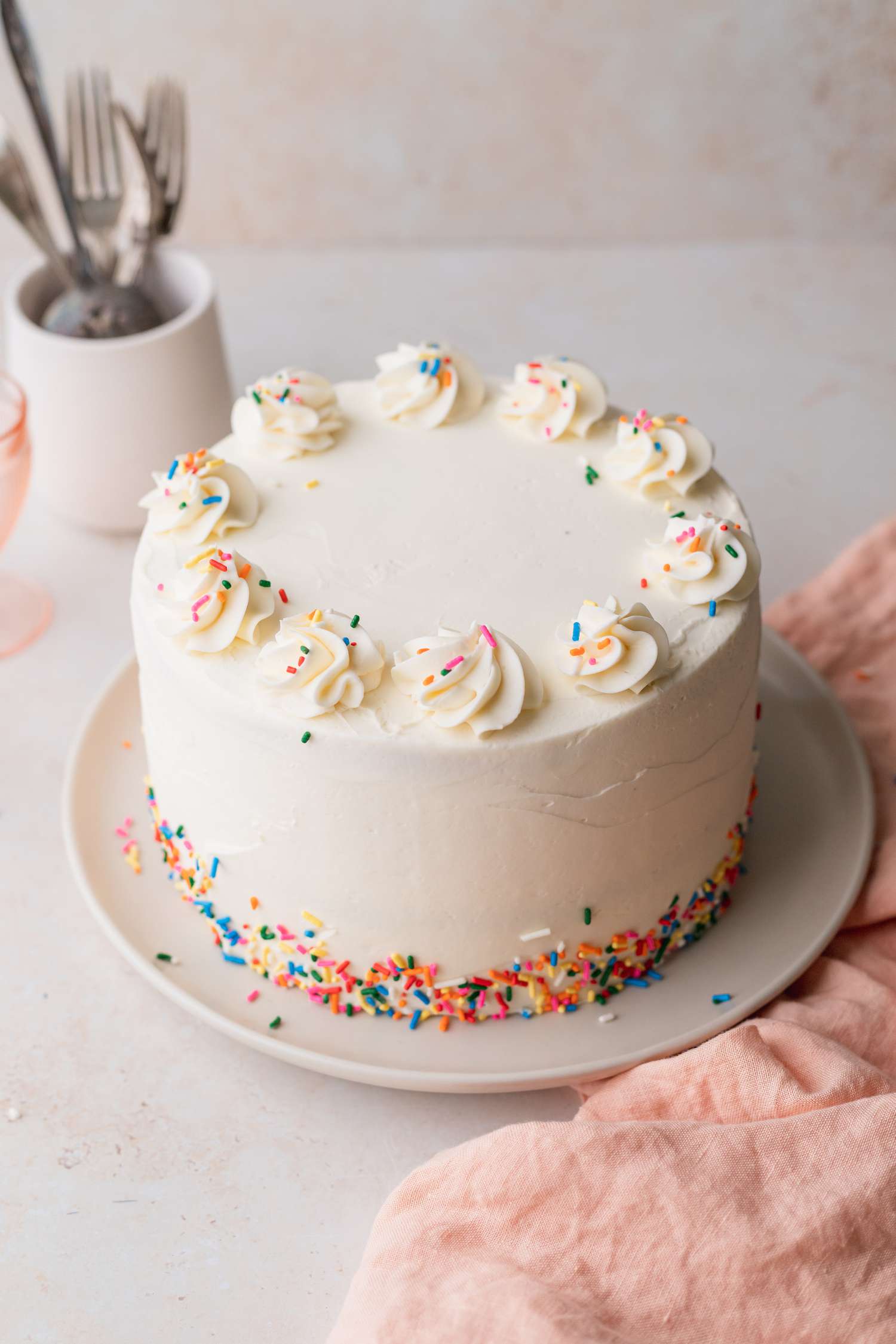 Decorated Rainbow Cake on a Plate with a Cup of Utensils in Background