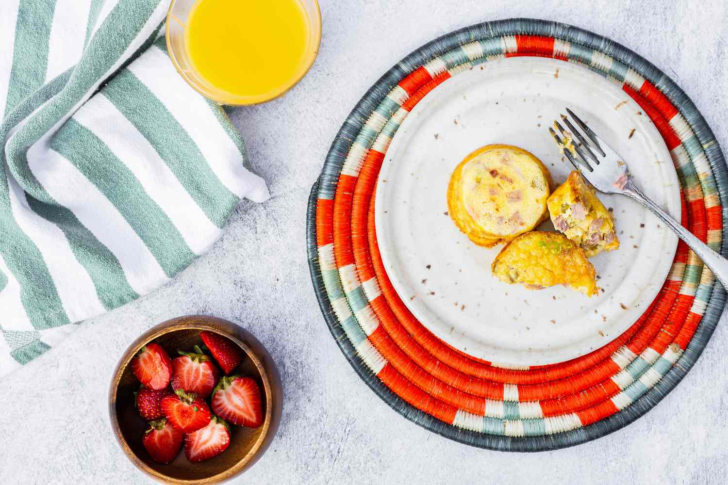 Ham, Cheddar, and Green Chile Egg Bites on a Plate Next to a Bowl of Strawberries and a Glass of Orange Juice