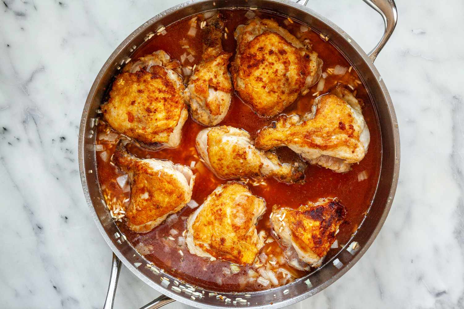Adding stock and tomato to a skillet for pollo chicken.