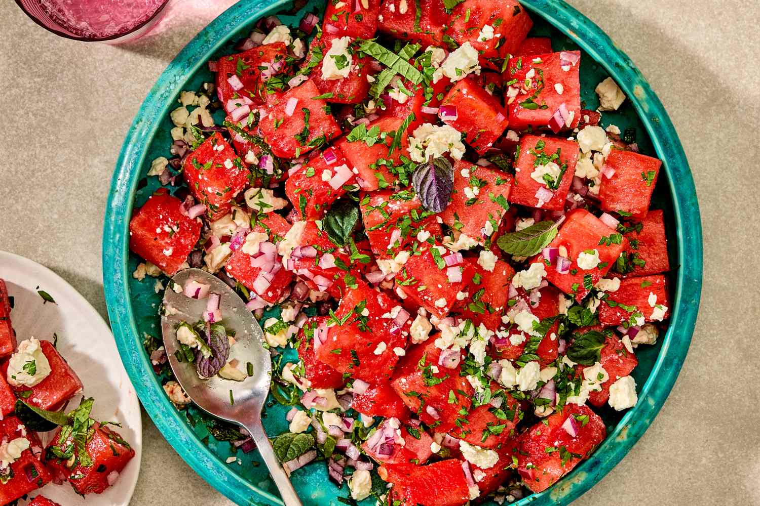 A watermelon and feta salad garnished with herbs in a blue bowl with a serving spoon