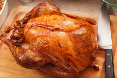 A whole roasted turkey on a wooden cutting board, with a chefs knife on the right side