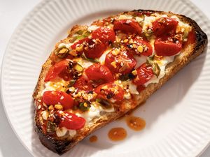 A slice of toast topped with roasted tomatoes cottage cheese and seasonings on a plate
