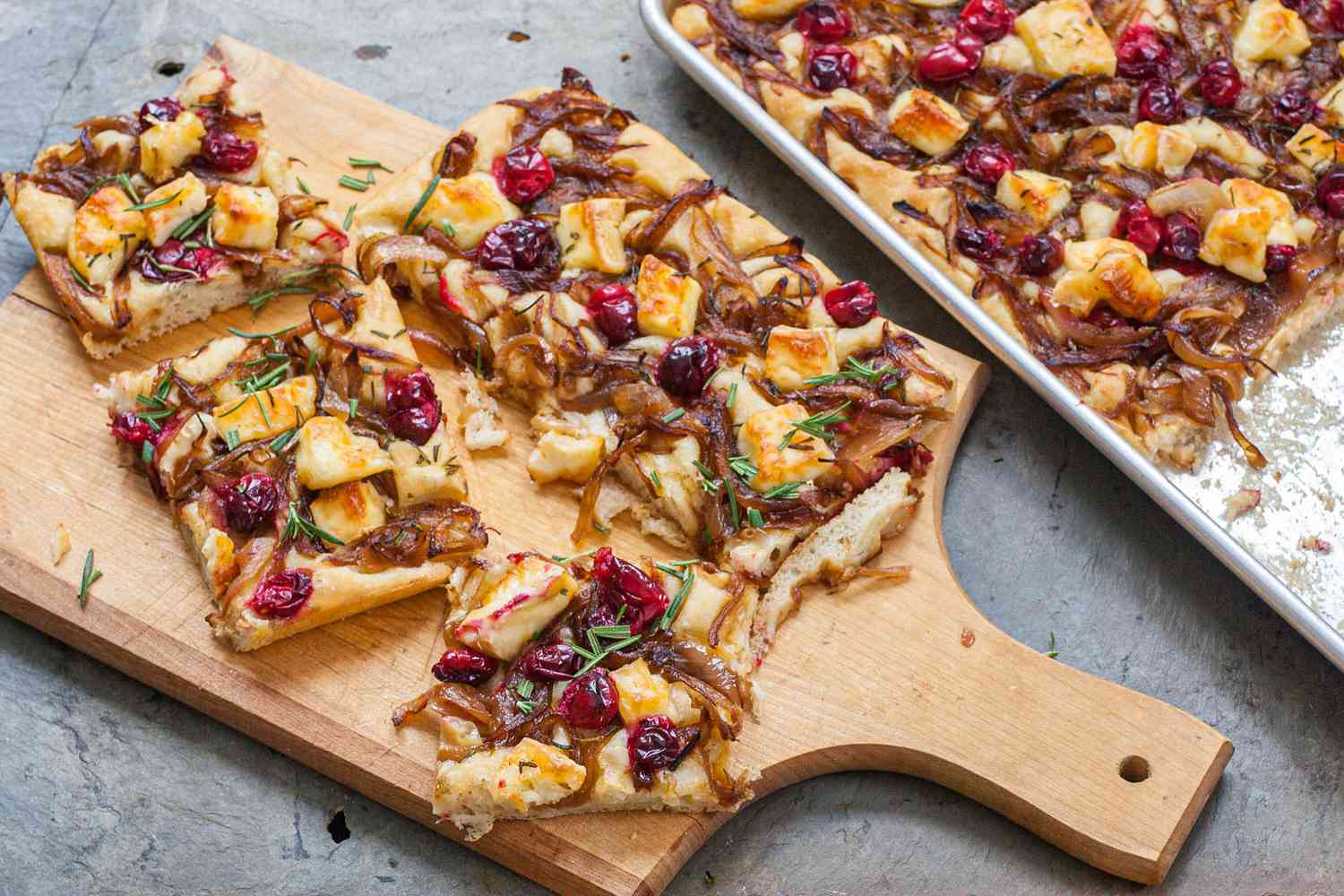 Slices of Focaccia with Caramelized Onions, Cranberries, and Brie on a Cutting Board, and Next to It, a Tray with More Focaccia 