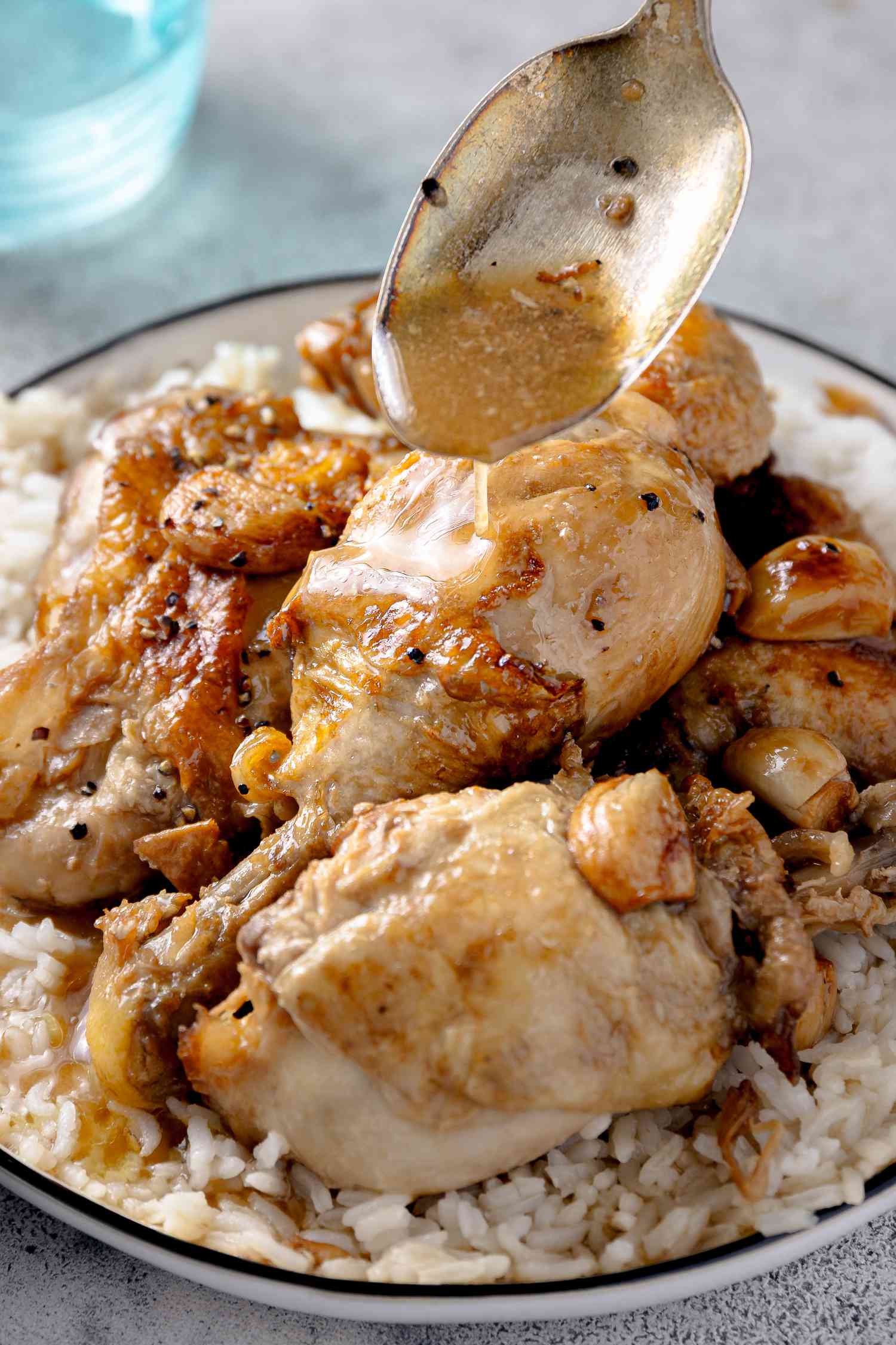 Spoonful of Sauce Poured onto Chicken Adobo in a Bowl of Rice 