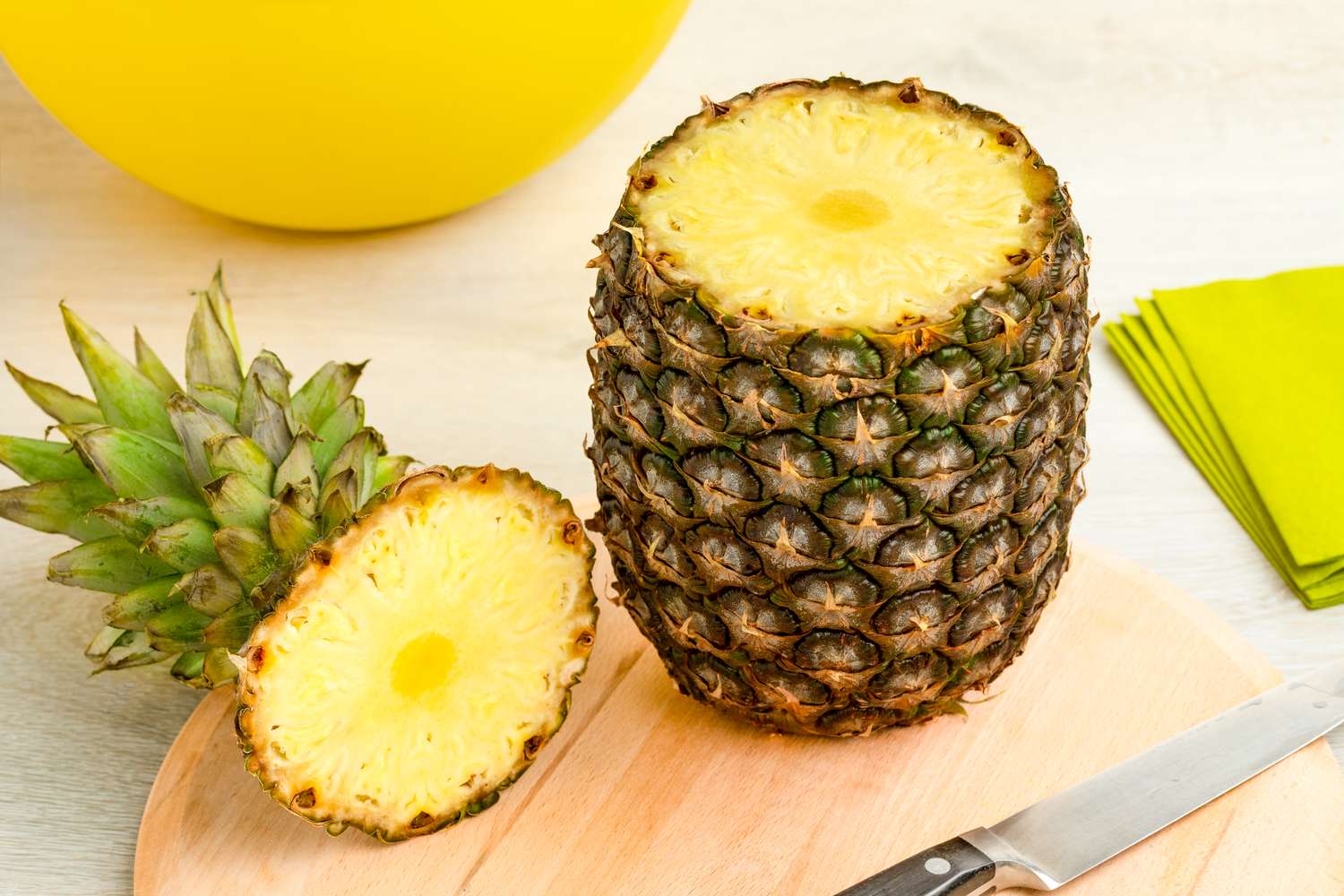 Pineapple with top removed showing interior flesh on a wooden cutting board with a knife nearby