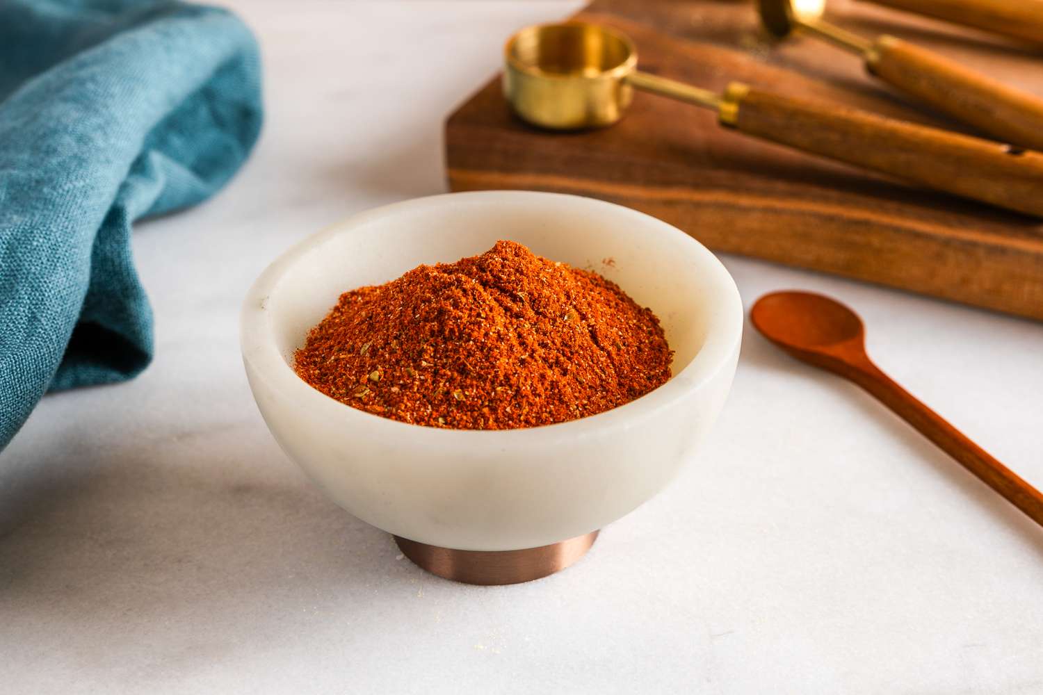 Small bowl of chili powder on a counter with measuring spoons and a small spoon